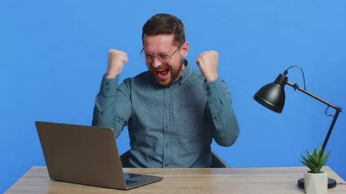 Excited Man Cheering at Desk Using Laptop