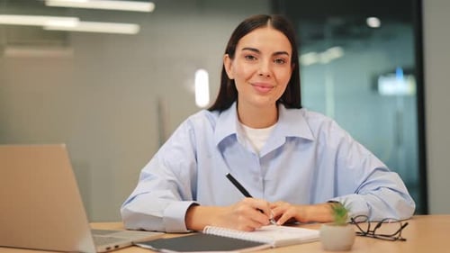 Happy Professional Woman Writing and Smiling at Office Desk