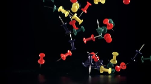 Colorful Thumbtacks Falling onto a Black Reflective Surface