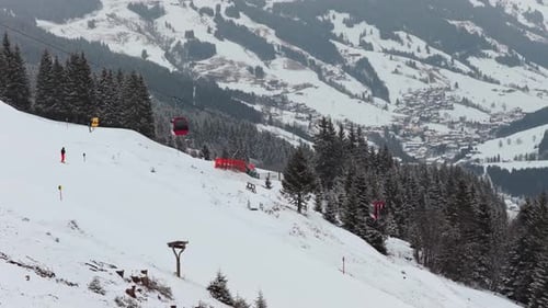 Skiers Ride Down Slope and Red Cable Car Ascende an Alpine Resort with a Mountain Village in the