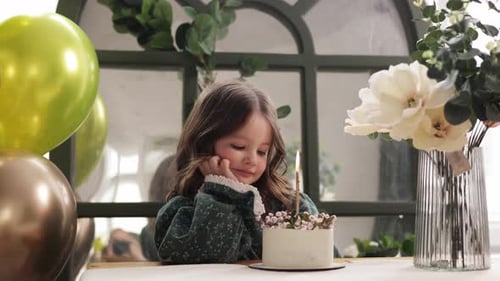 Child birthday party. Adorable little girl sits by the table with birthday cake decorated flowers