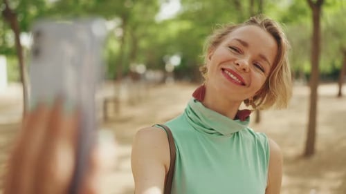 Woman Smiles and Takes Selfie in Sunny Park