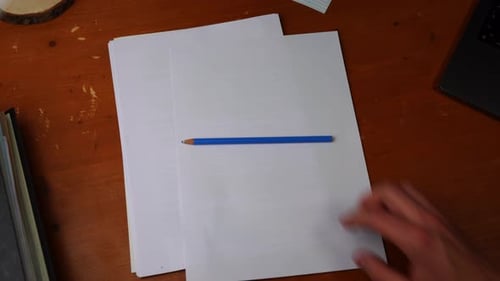 blue crayon is placed on a piece of paper on a wooden desk by a youthful right hand, then grabbed it