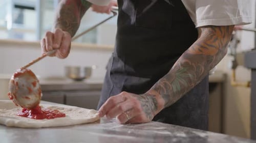 Chef Adding Tomato Sauce with Ladle to Pizza Base