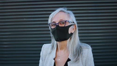 Senior businesswoman in face mask stands on city terrace during covid-19 pandemic