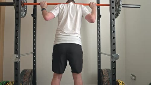 Static shot of a man unracking the bar and starting to squat the weight