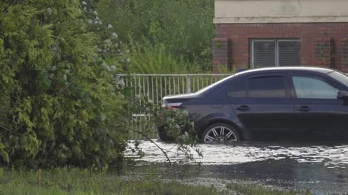 Submerged Car on Flooded Road with Trees Nearby After Flash Flood Caused by Heavy Rainfall.