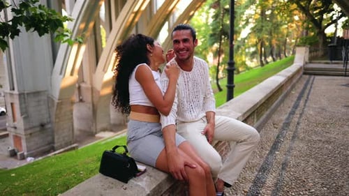 Romantic young interracial couple sitting on a stone wall in a park, laughing and enjoying a beautif