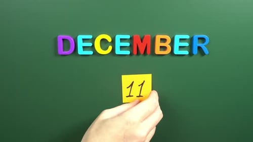 Hand sticking a sticker 11 December calendar day on school board. 11 date of December. Eleventh