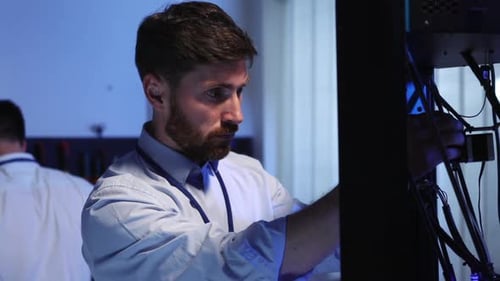 Joven trabajador técnico barbudo caucásico que realiza la reparación de una impresora tridimensional coworking