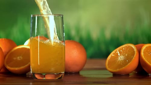Orange Juice Being Poured Into Glass with Oranges