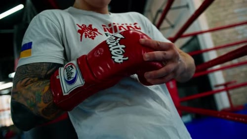 Athletic Boxer Putting on Red Boxing Gloves in Gym