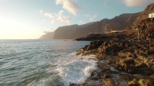 Jagged coastal rocks backlit by the soft light of a setting sun, with the ocean stretching out to a
