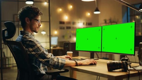 Fin de soirée au bureau créatif : un photographe professionnel travaille sur un ordinateur de bureau avec deux Gre