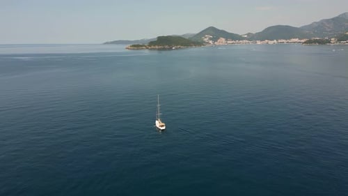Aerial View of a White Yacht Sailing in the Open Sea Against the Backdrop of Distant Shores and