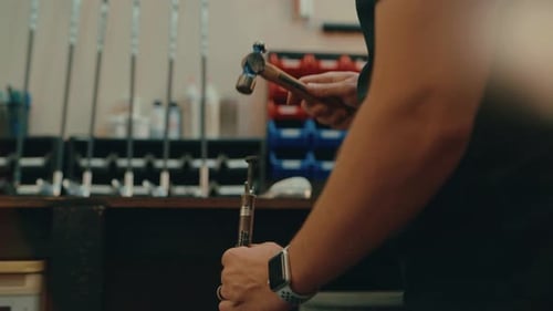 Male hands hammer nail into golf club shaft for custom fitting in workshop in slow motion