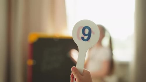Young Girl with Paddle Number Nine in Classroom