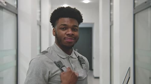 Smiling Young Man Holding Laptop in Office Hallway