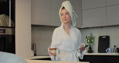 Woman in Robe with Coffee and Phone in Kitchen