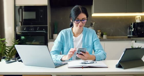 Woman Works on Cellphone at Kitchen Table