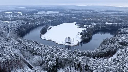 Flying above snowy forest and river in winter