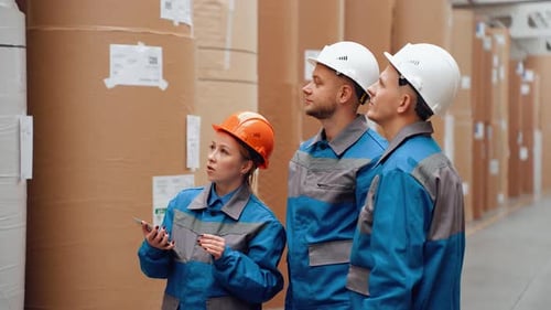 Workers Inspecting Large Paper Rolls in Warehouse