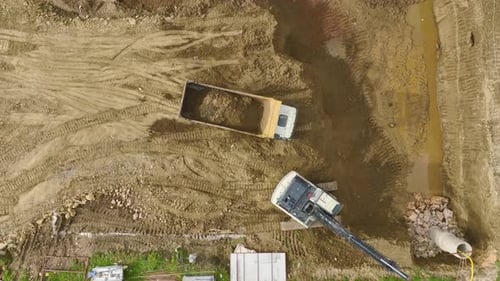 Aerial Video Aerial View of an Excavator at a Construction Site Digging and Transferring Soil Into a