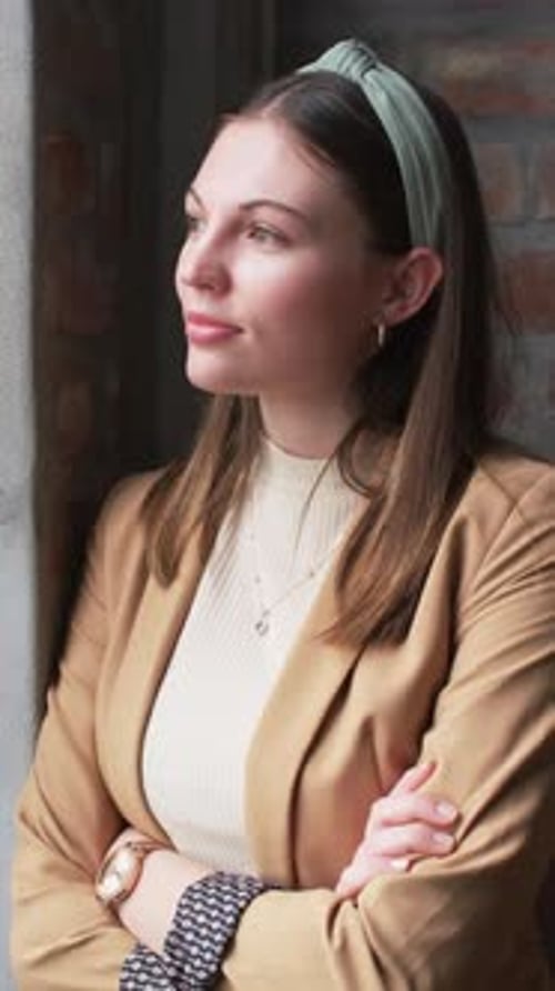 Vertical video: Businesswoman in blazer standing with arms crossed, smiling confidently in office