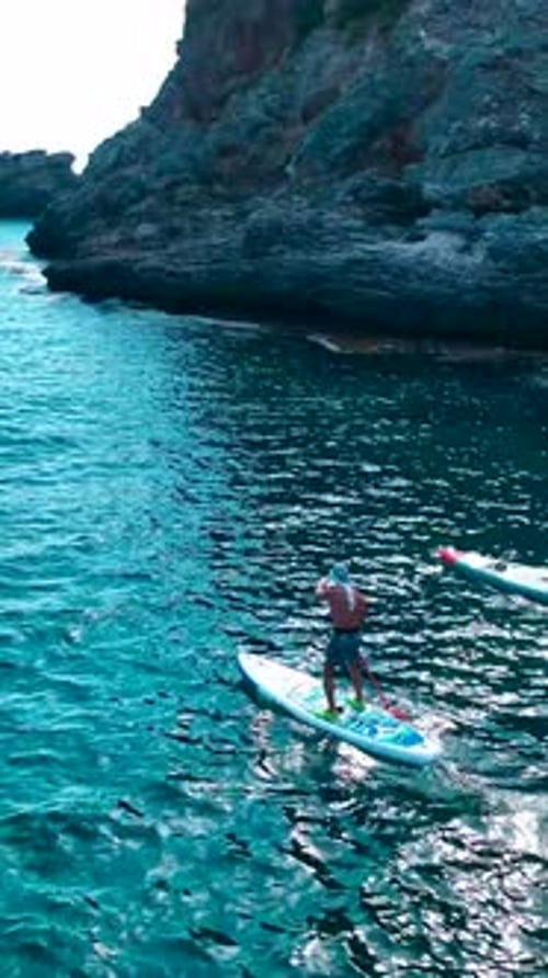 Vertical Video People Paddleboard Along Rocky Mediterranean Shores Enjoying Relaxation and Stunning