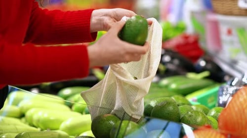 Mujer recogiendo aguacates en una bolsa reutilizable en una tienda. Temáticas del Día de la Tierra y la Ecología