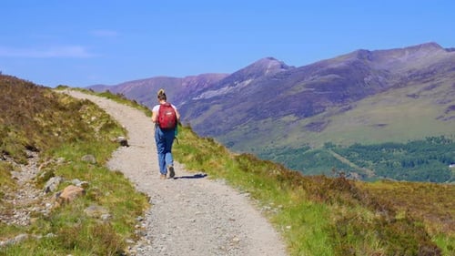 Following a backpacking hiker walk on a trail with sweeping mountain views of the Scottish Highlands
