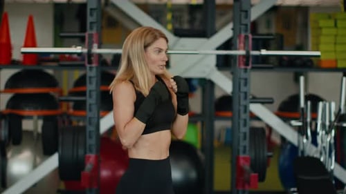 Aktive Frau mittleren Alters Boxen im Fitnessstudio Interieur Punching Air mit eingewickelten Bändern Fäusten Zeitlupe