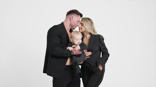 Caucasian couple wearing black suits with their infant kid. Happy family of three studio footage.
