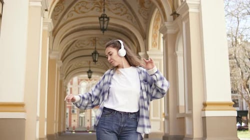 Pretty Young Woman Putting on Headphones Listening Music and Dancing