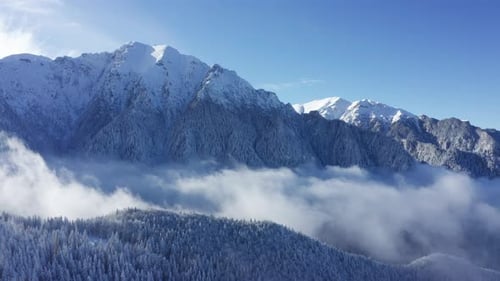 Snow-capped Bucegi Mountains towering above clouds, serene winter landscape
