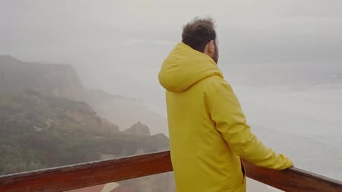 Lone Man in Yellow Raincoat Overlooking Misty Coastline
