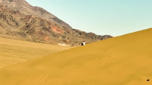 Person sitting on a vast desert dune with distant mountains