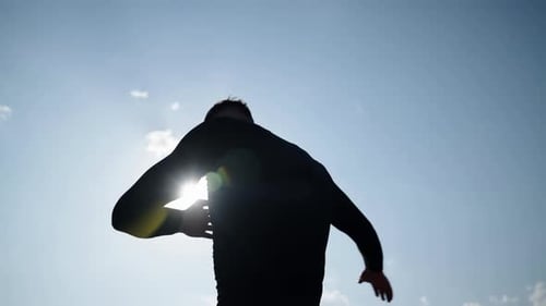 The Athlete Does a Sports Warmup and Spreads His Arms Wide Against the Background of the Bright Sun