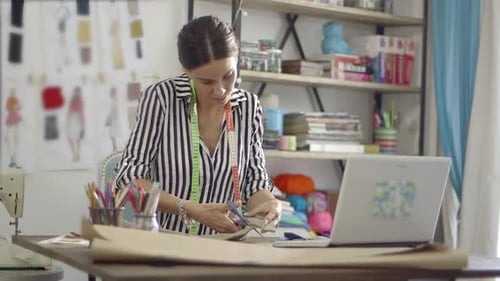 Young female fashion designer working at home studio cutting fabric.