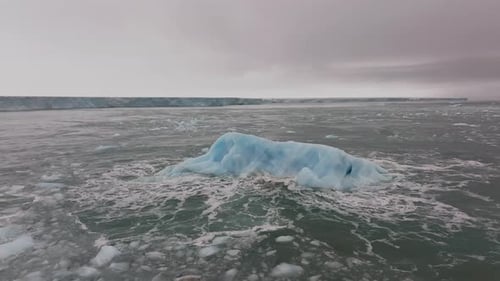 Iceberg floating in the Arctic ocean with massive ice shelf in the horizon, Aerial view