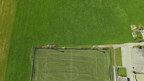 Aerial video shows an empty soccer field with visible pitch lines surrounded by lush green farmland.