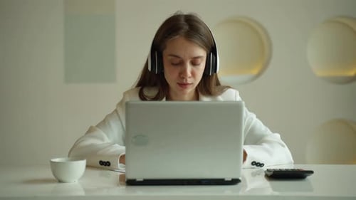 Smiling Woman Wearing Wireless Headphones Makes a Video Call on Her Laptop Computer in the Office