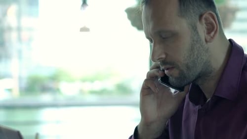 Young man chatting on cellphone and using laptop in cafe in the city