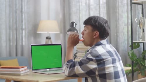 Bored Asian Teenager Yawning With Green Mock Up Screen Laptop While Doing Home Work