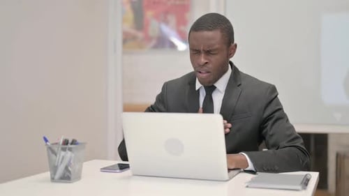Coughing African Businessman Using Laptop while Sitting in Office