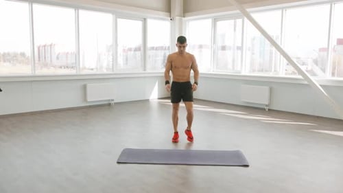 Jeune homme musclé en short noir faisant des levées de jambes et des sauts dans la salle de fitness