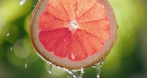 Grapefruit Slice with Cascading Water on Green Background