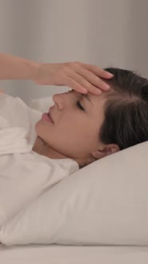 Woman Lying in Bed Touching Forehead