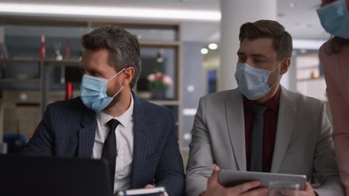 Diverse coworkers in face masks discuss business development strategy in the office