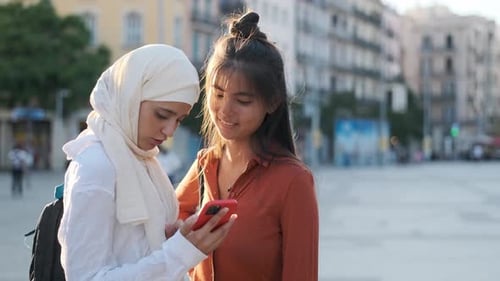 Two Young Multiethnic Female Friends Using a Mobile Phone While Standing Outdoors on the Street